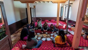 A group of people sitting on patterned rugs in a room with wooden beams on the ceiling.
