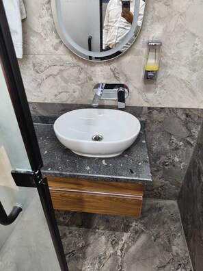 Un bany amb un mirall rodó, un lavabo blanc i una paret amb mosaic de marbre.