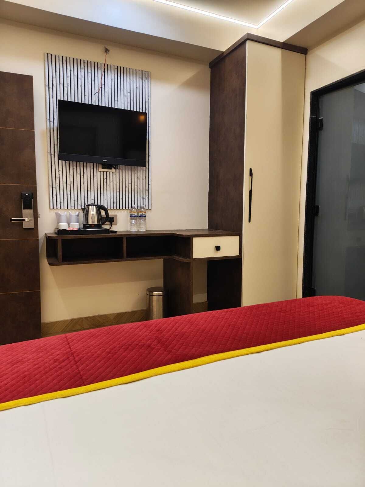 A hotel room with a bed, a desk with a flat-screen TV, a minibar, and a wardrobe.