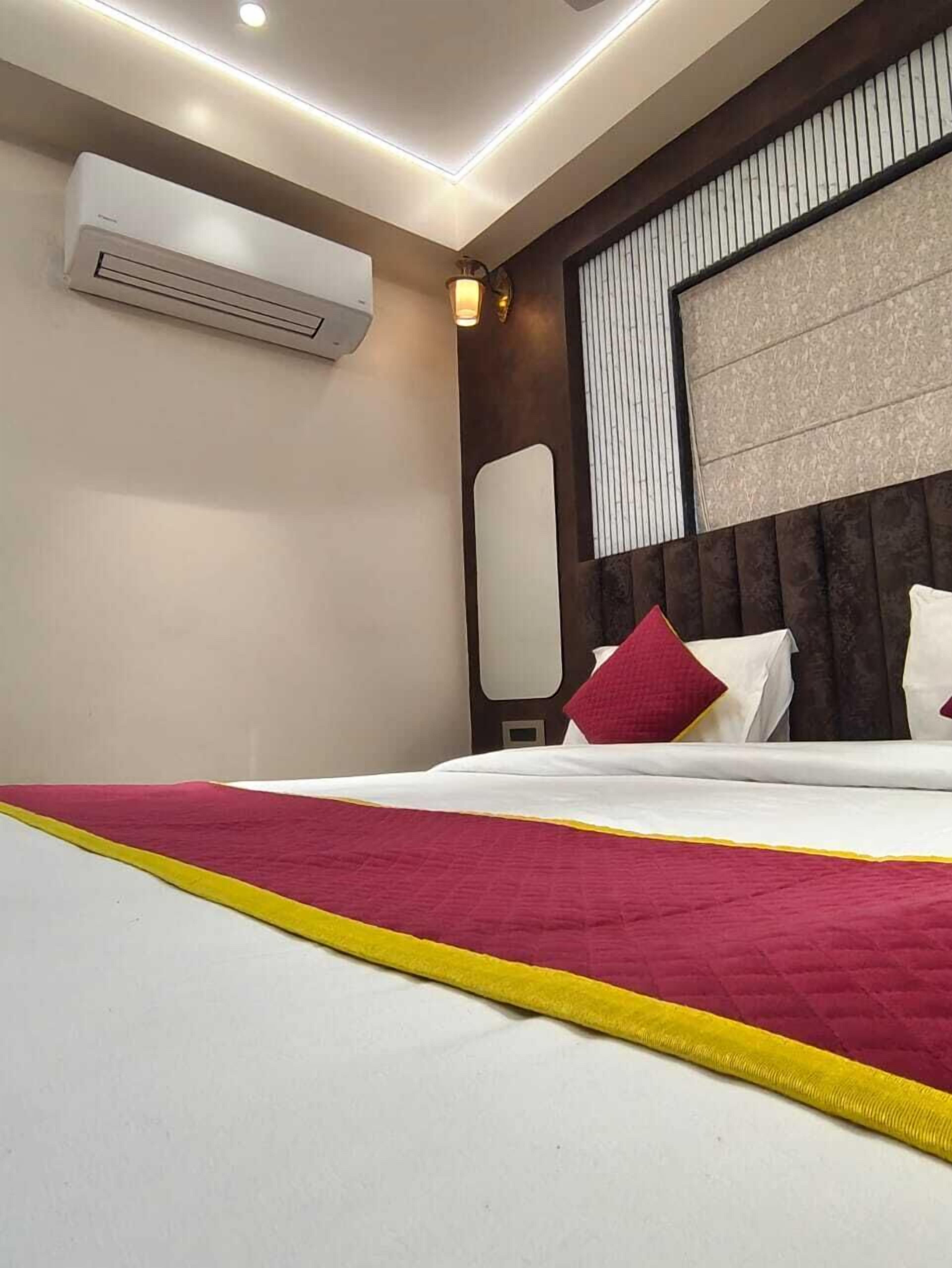Quarto de hotel com cama, ar-condicionado na parede, abajur e janela com persianas.