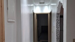 A narrow hallway with white walls, recessed lighting, and a tiled floor.