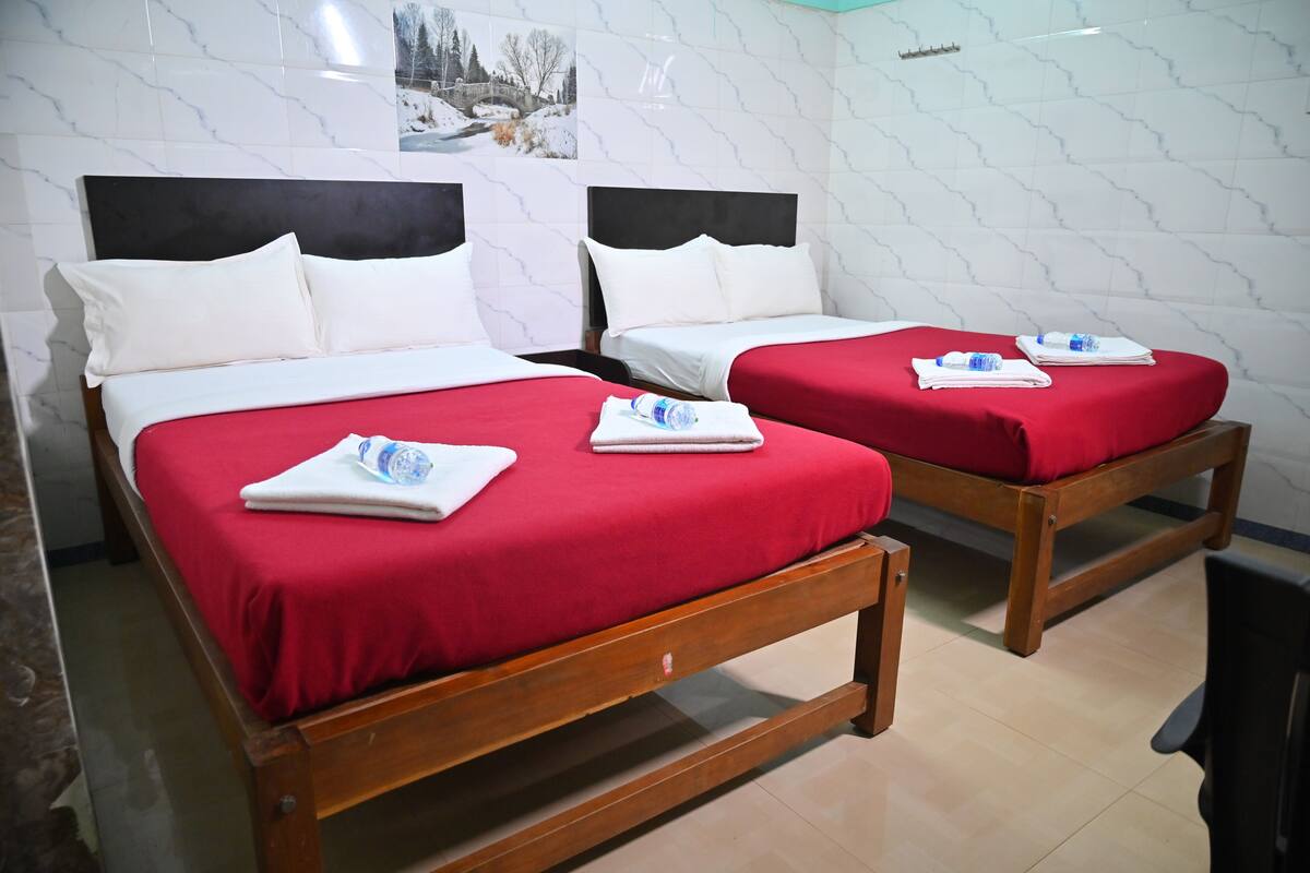 Two wooden beds with red bedding and white pillows, each with a folded towel and a water bottle.