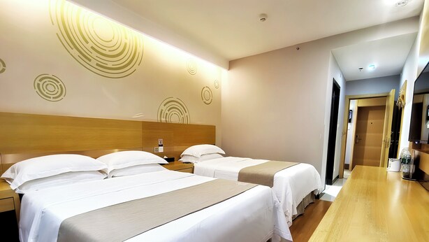 A hotel room with three beds, a wooden headboard, a long wooden table, and a wall with circular patterns. - Gelin Haotai Zhixuan Jiudian (Shunyi)