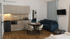 A compact living space with a kitchenette, a dining area, a sofa, and a TV mounted on the wall. - Aenaon Corfu Luxury Apartments 04 - Aphrodite Apt (Corfu)