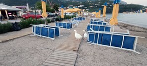 A beachside area with blue and yellow beach chairs, a wooden walkway, and a view of the sea. - Aenaon Corfu Luxury Apartments 05 - Athena Apt (Corfu)