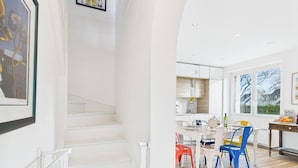A modern kitchen with white cabinetry, a dining area with colorful chairs, and large windows offering a view of the outdoors. - -Alizée- Charming house in Névez (Névez)