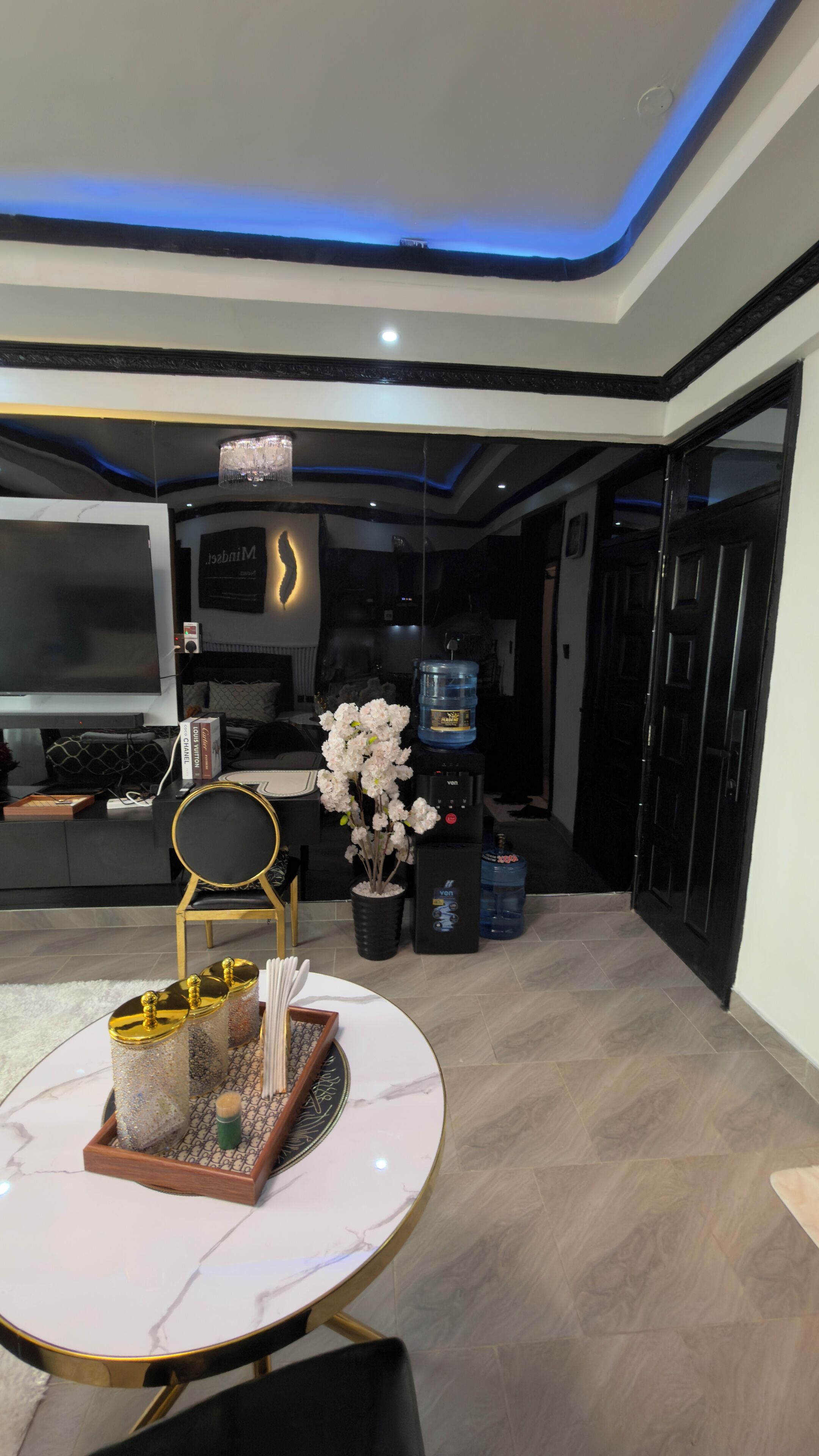 Un soggiorno moderno con televisore, un lampadario, un distributore d'acqua e un tavolo da pranzo con oggetti decorativi.