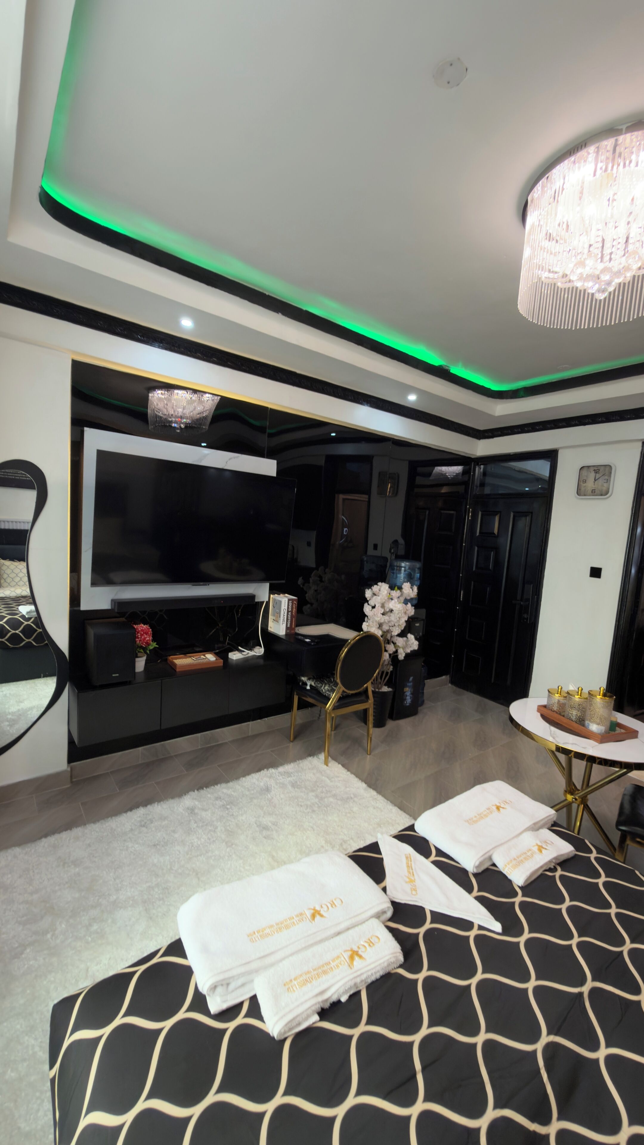 Una camera d'hotel moderna con una grande TV a schermo piatto, un lampadario, uno specchio rotondo e un letto con asciugamani.