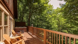 Een houten terras met buitenmeubilair en een hottub, omringd door weelderige begroeiing.