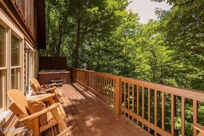Eine Holzterrasse mit Sitzgelegenheiten im Freien und einem Whirlpool, umgeben von üppigem Grün.