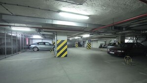 A multi-level underground parking garage with concrete pillars, fluorescent lighting, and metal railings. - Economy Studio in Strong Center of Belgrade with Private Garage (Beograd)
