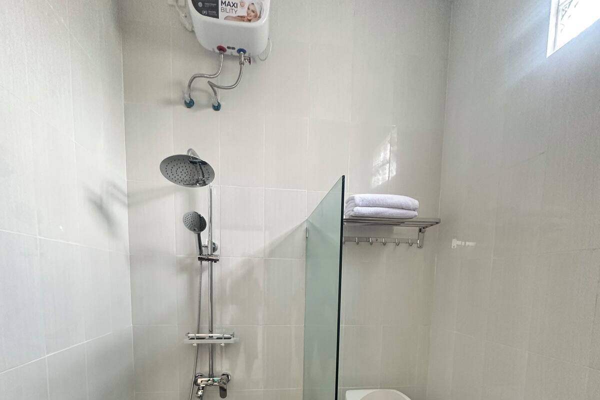 A bathroom with a toilet, shower, and a soap dispenser mounted on the wall.