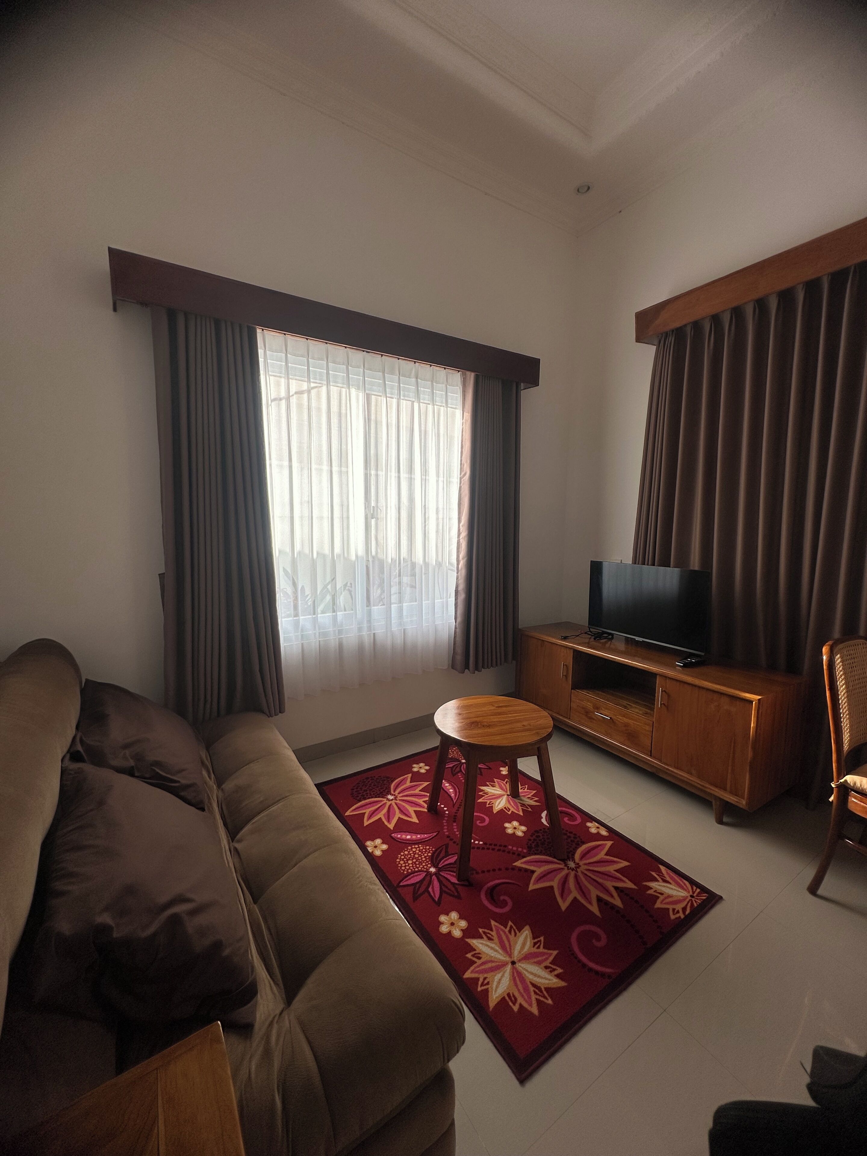 Una sala de estar con un sofá, un televisor sobre un mueble de madera, un taburete pequeño y un tapiz estampado.