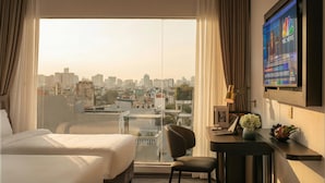 A hotel room with a large window offering a city view, a desk with a laptop, and a television displaying NBC News. - Sora Hotel Hanoi (Hanoi)