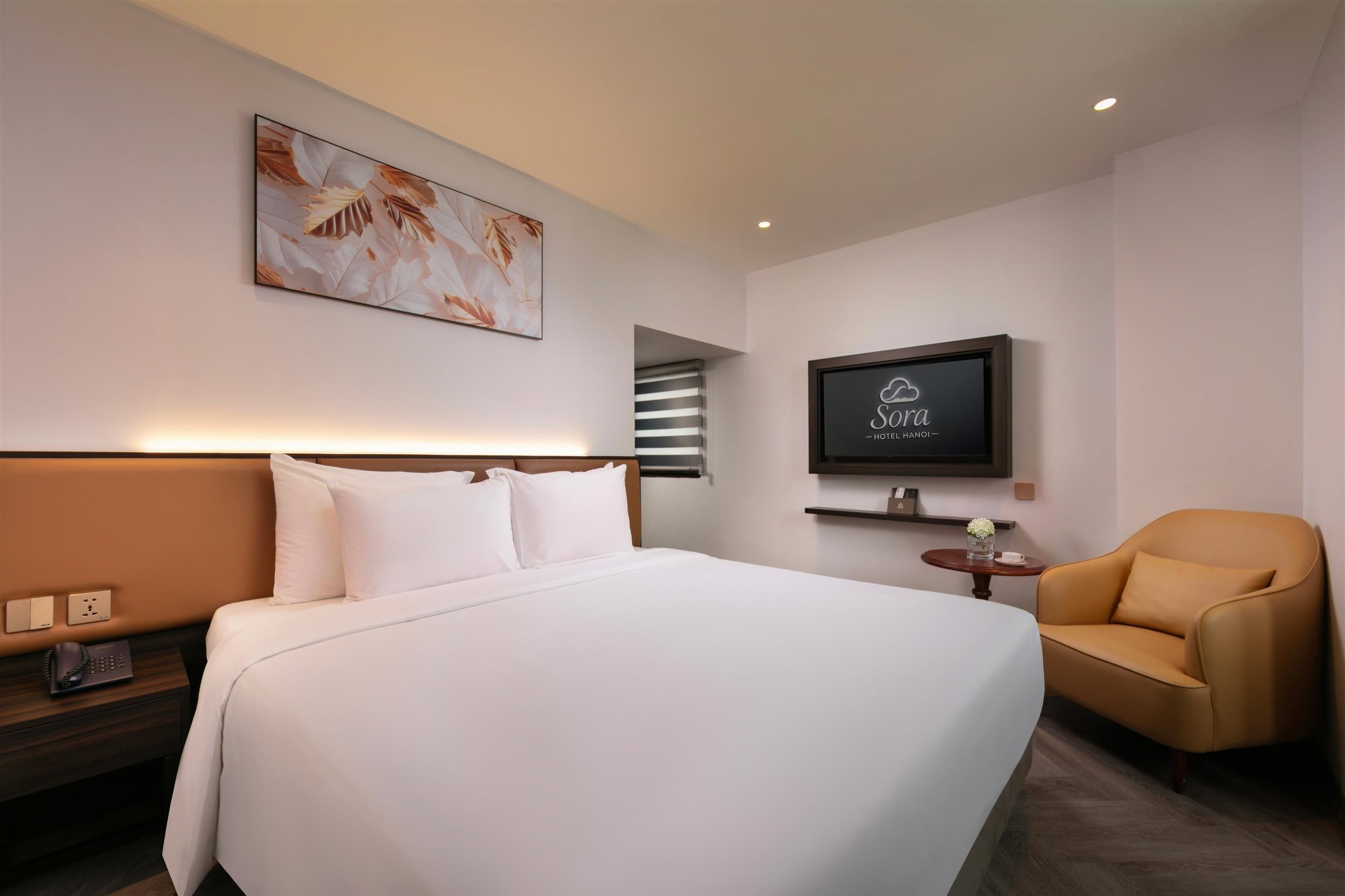 A hotel room with a bed, a chair, a television, and a wall-mounted artwork.