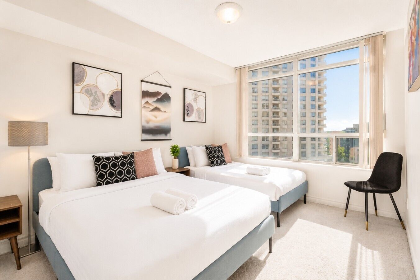 A hotel room with two beds, a desk, a chair, and a large window with a city view.