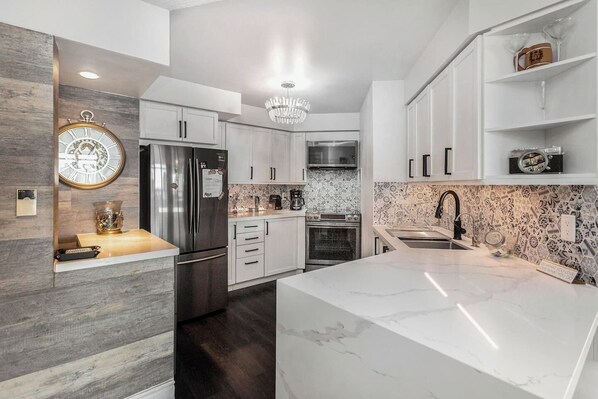 A modern kitchen with white cabinetry, a marble island, a stainless steel refrigerator, and a decorative clock.