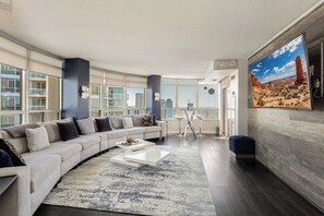 A modern living room with a large sectional sofa, a coffee table, and a large window offering a city view.