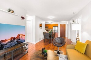 A modern living room with a flat-screen TV, a dining area, and a kitchen in the background.