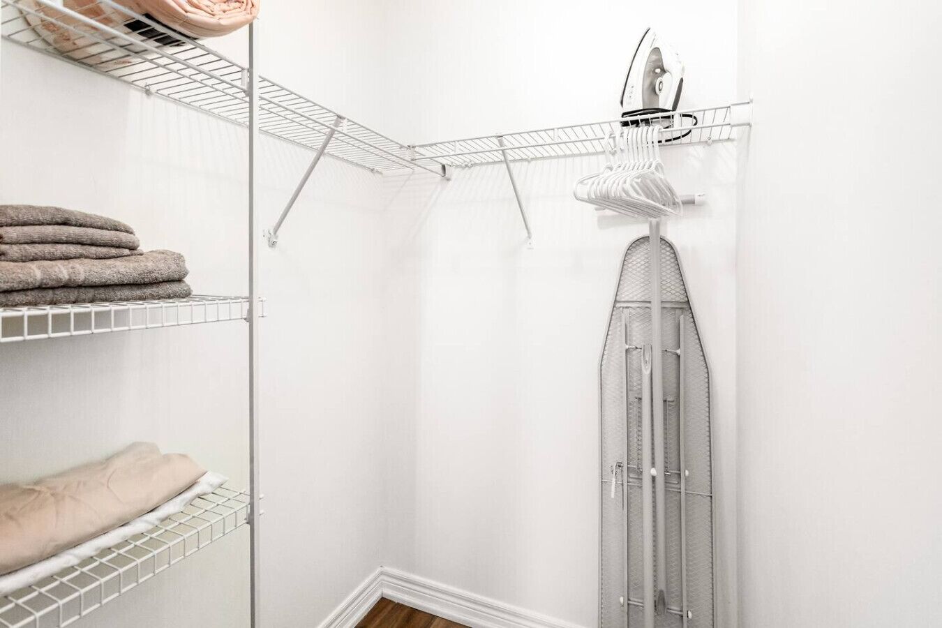 A corner laundry area with shelves for folded towels and a hanging rack for clothes.