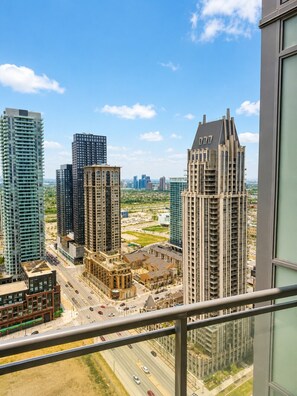 A high-rise building with a modern architectural design, a busy street below, and a clear sky. - Penthouse 2BR+Den | Skyline Views • SQ1 • Parking (Mississauga)