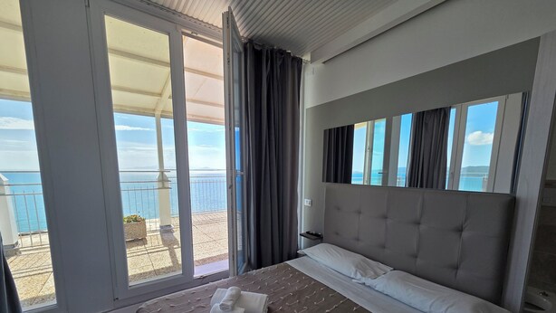 A hotel room with a large bed, a view of the sea, and a balcony with a railing. - Suite Torre Azzurra B&B Rooftop Sea View (Follonica)