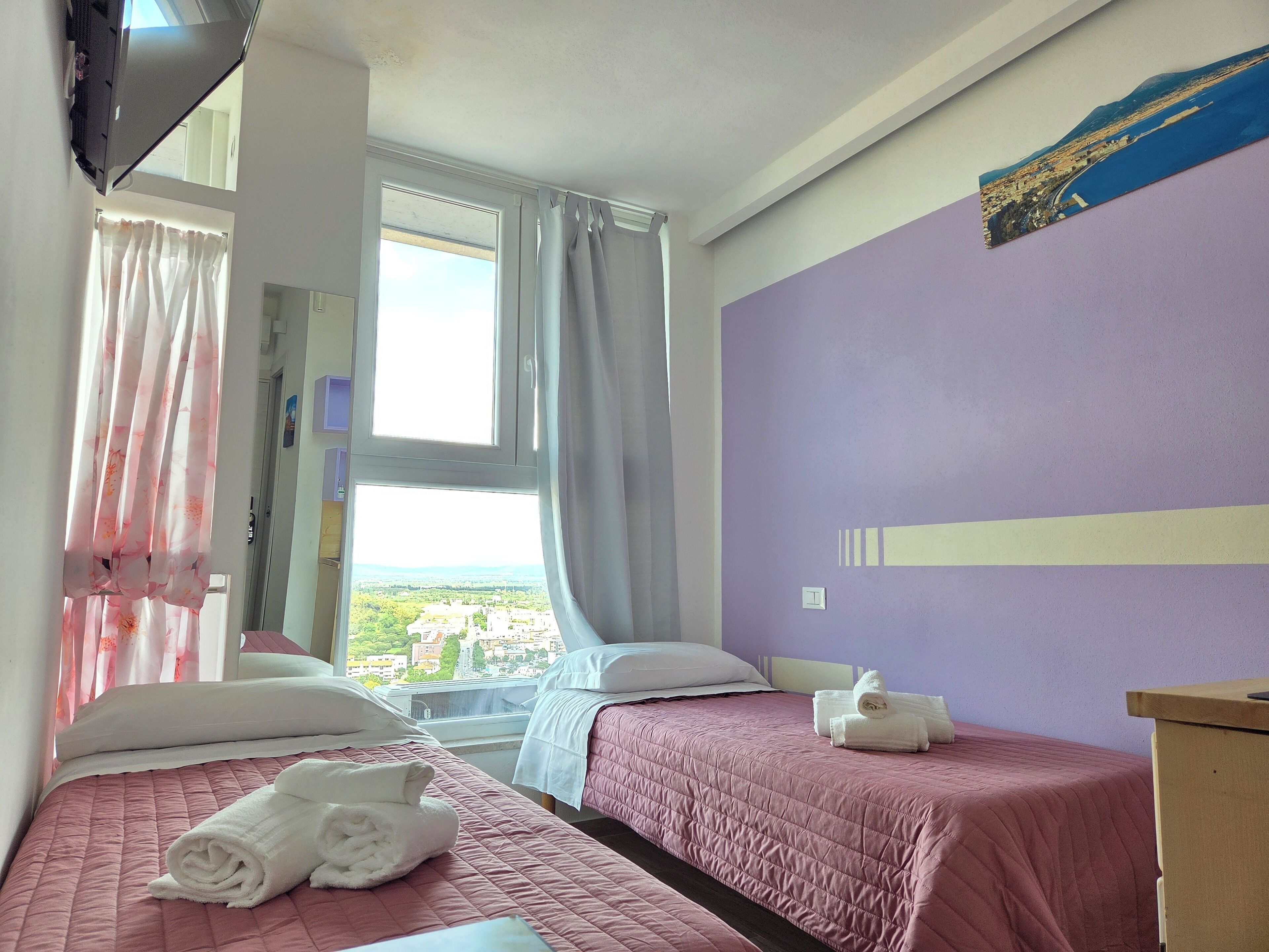 Una habitación de hotel con dos camas, una ventana con cortinas, una cama con una toalla enrollada y una pared con un cartel.