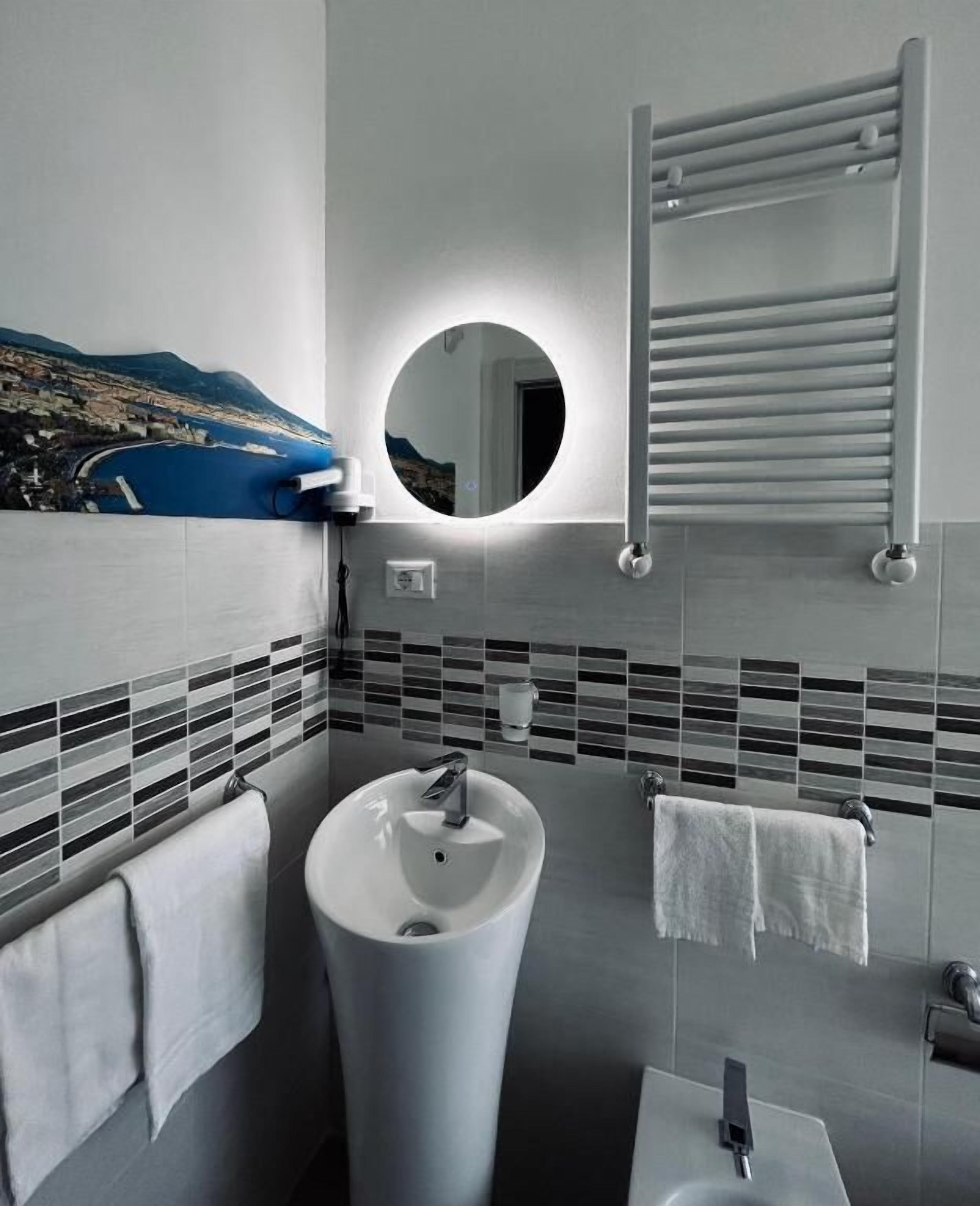 A modern bathroom with a large sink, a round mirror, and a towel rack.
