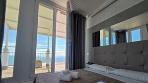 A hotel room with a large bed, a balcony with a view of the sea, and a sliding glass door. - Suite Torre Azzurra B&B Rooftop Sea View (Follonica)