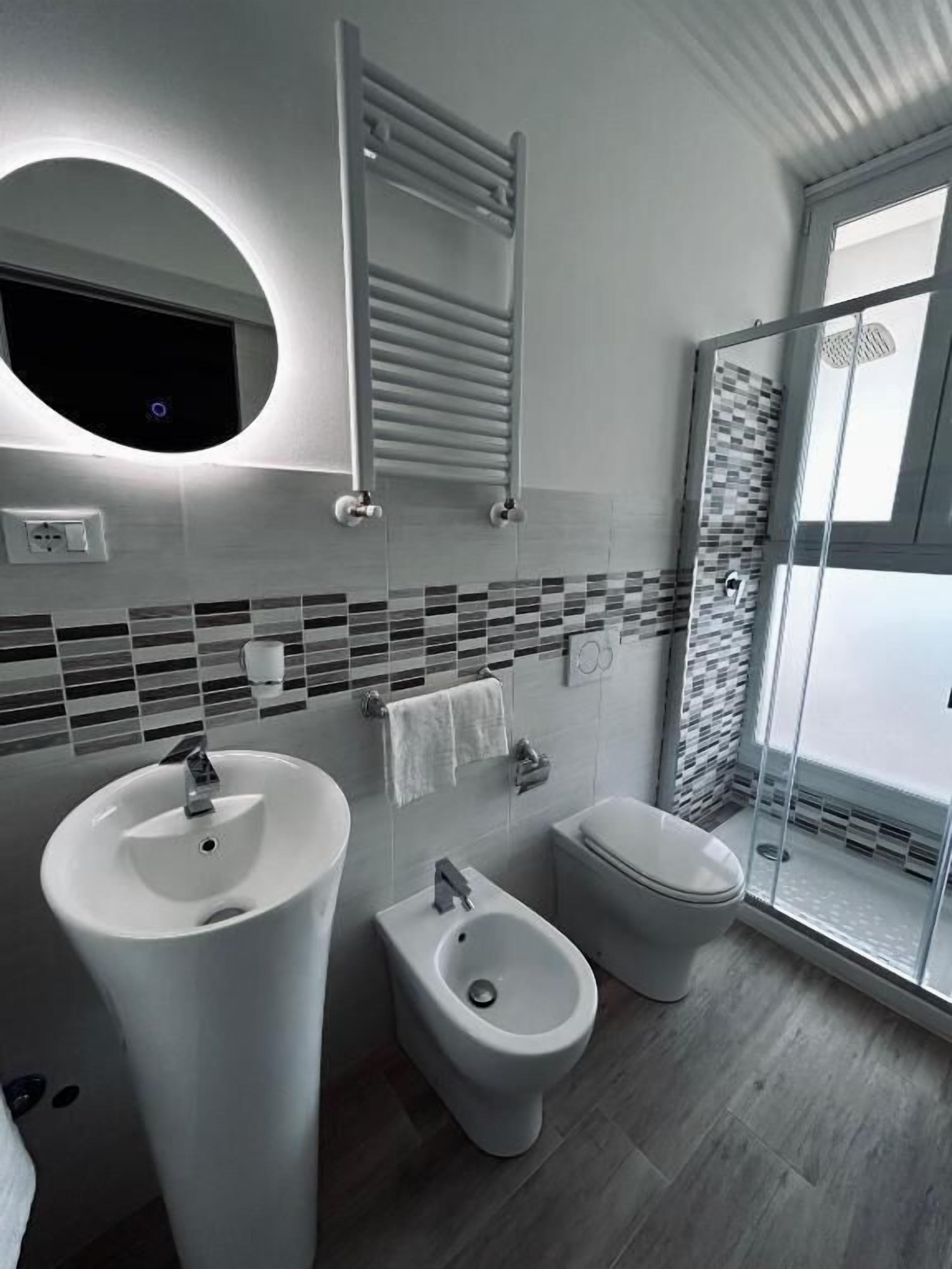 A modern bathroom with a large sink, bidet, toilet, and a glass-enclosed shower.