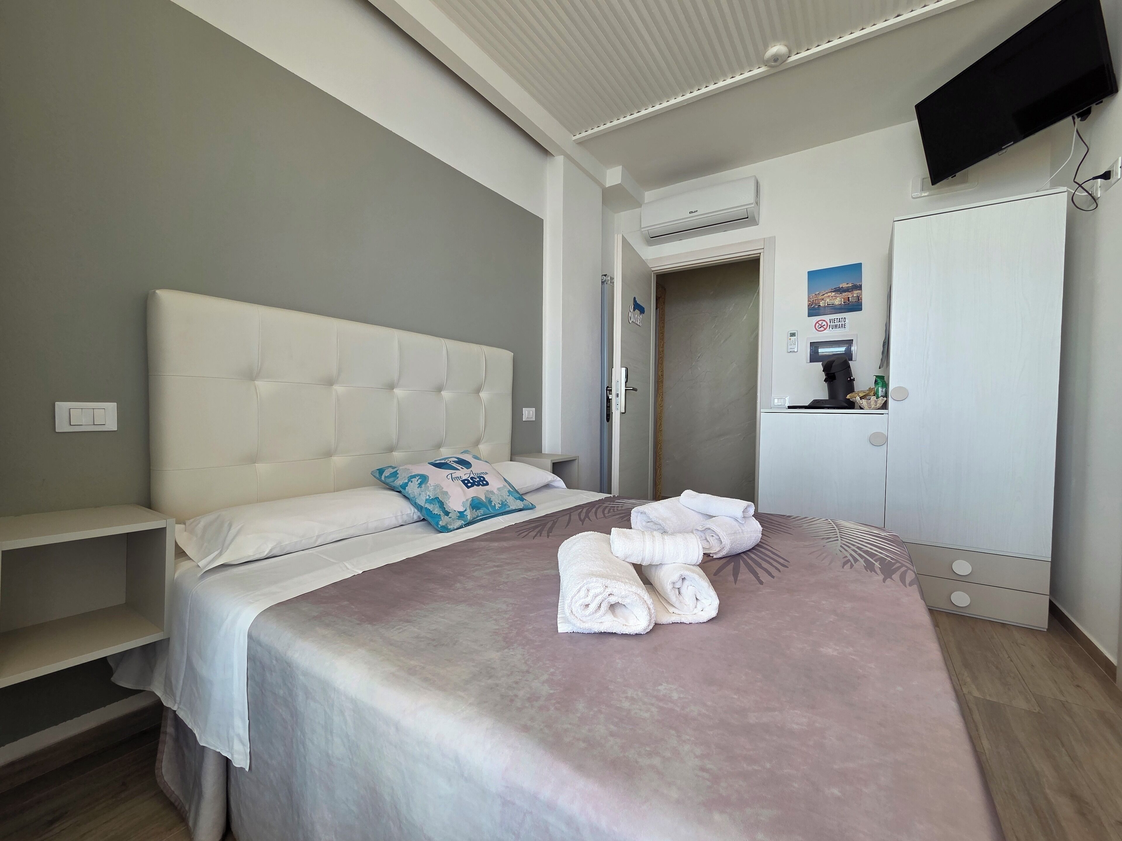 Hotellihuone, jossa on sänky, televisio, ilmastointilaite, vaatekaappi ja suihkutila.