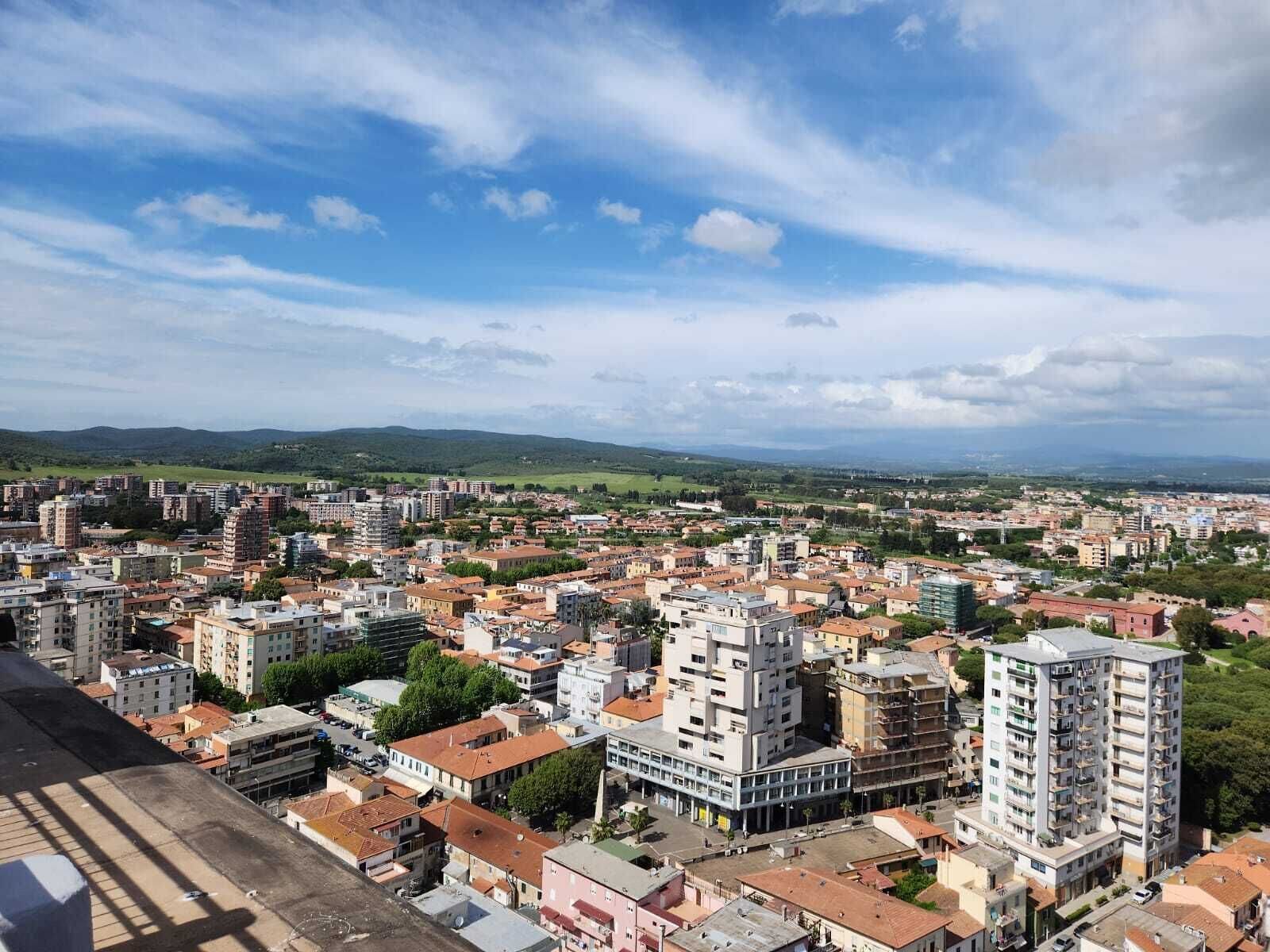 A cityscape with a mix of residential and commercial buildings, including high-rise apartments and smaller houses, under a partly cloudy sky.