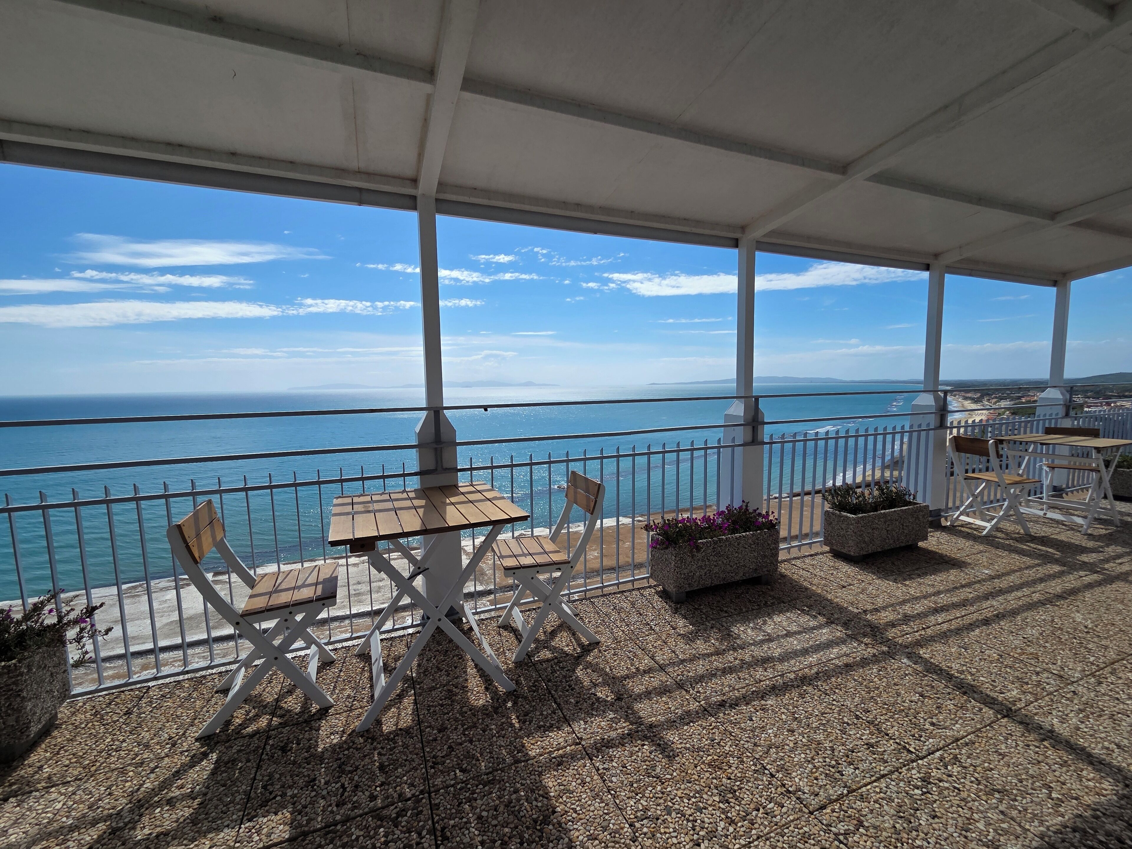Une terrasse couverte, dotée de tables et de chaises, qui offre une vue sur la côte.