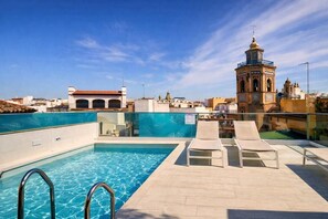 A rooftop pool with clear blue water, lounge chairs, and a view of a historic tower. - LA GIRALDA VIEWS APARTMENTS, with roof terrace and pool! (Sevilla)