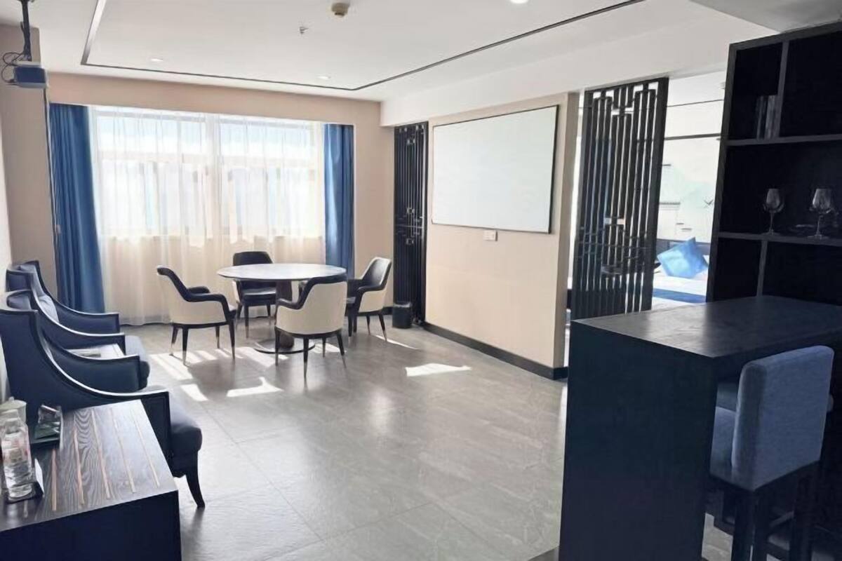 Una habitación de hotel moderna con una mesa redonda, sillas, una pantalla grande y una estantería.