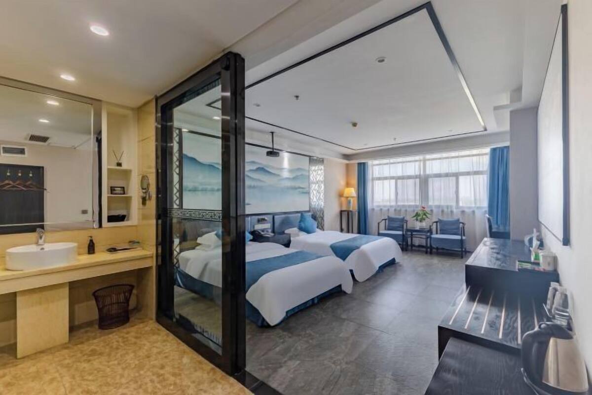 Una habitación de hotel con una cama grande, un escritorio, un baño con lavamanos y un ventanal amplio.