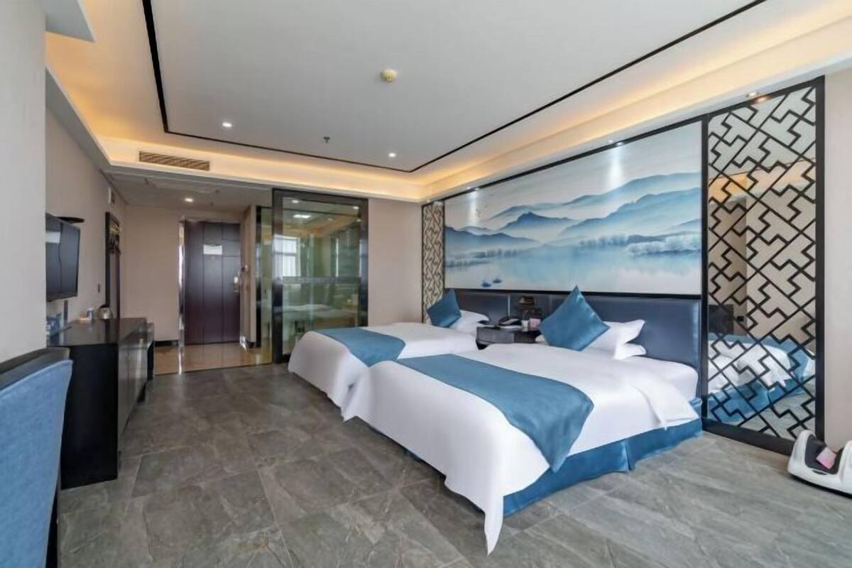Una habitación de hotel con dos camas, un escritorio y un amplio ventanal con vistas a las montañas.