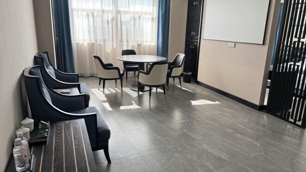 A conference room with a round table, six chairs, a projector screen, and a black partition.