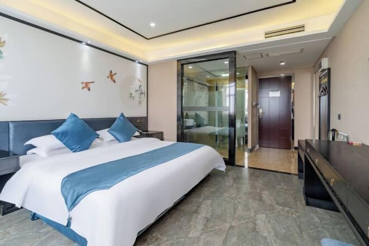 Una habitación de hotel moderna con una cama grande, un escritorio y una puerta de vidrio que da a un baño.