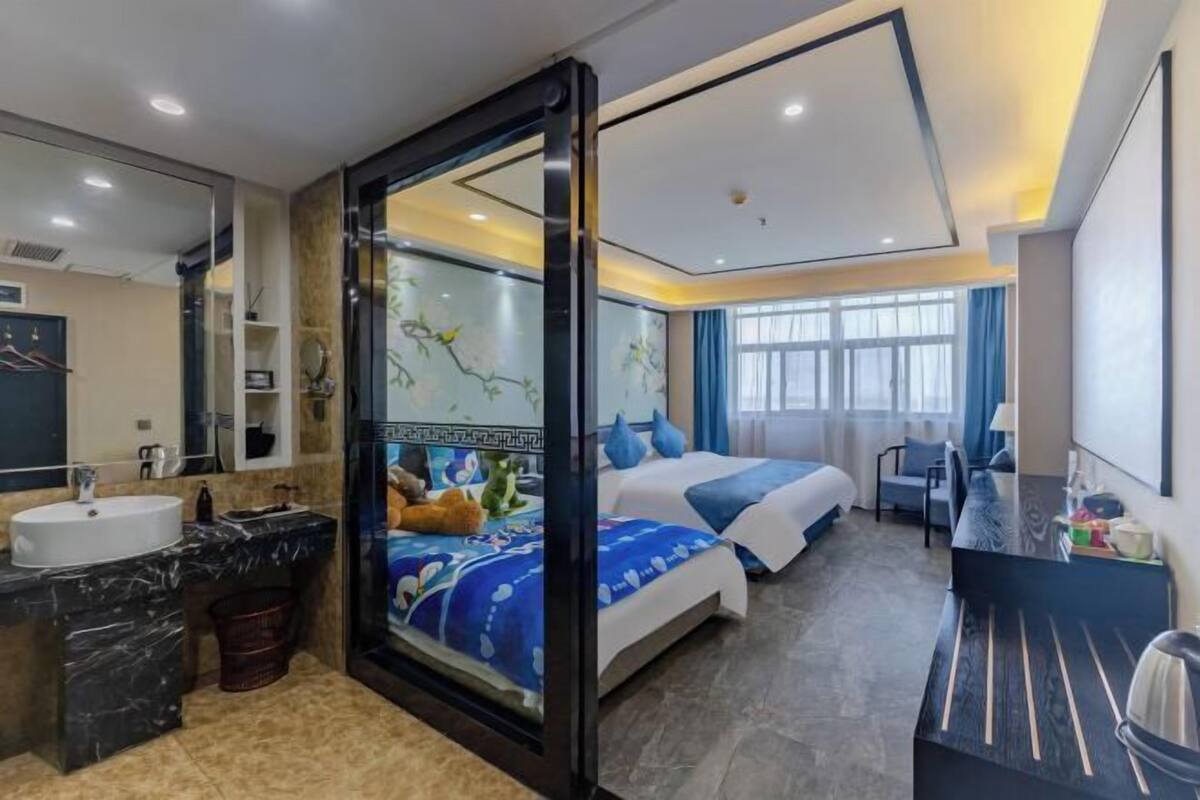 Una habitación de hotel con baño, cama, escritorio y un ventanal grande.