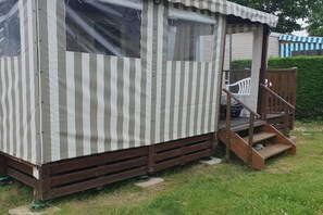 En liten, randig träbyggnad med en veranda och några trappsteg.