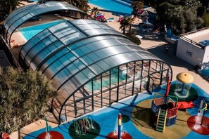 En stor, böjd glasstruktur med en pool inuti, omgiven av ett färgglatt lekområde med rutschkanor och vattenattraktioner.