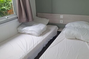 Ett litet, rent rum med två enkelsängar, ett fönster med gardiner och en vägg i en ljus färg.