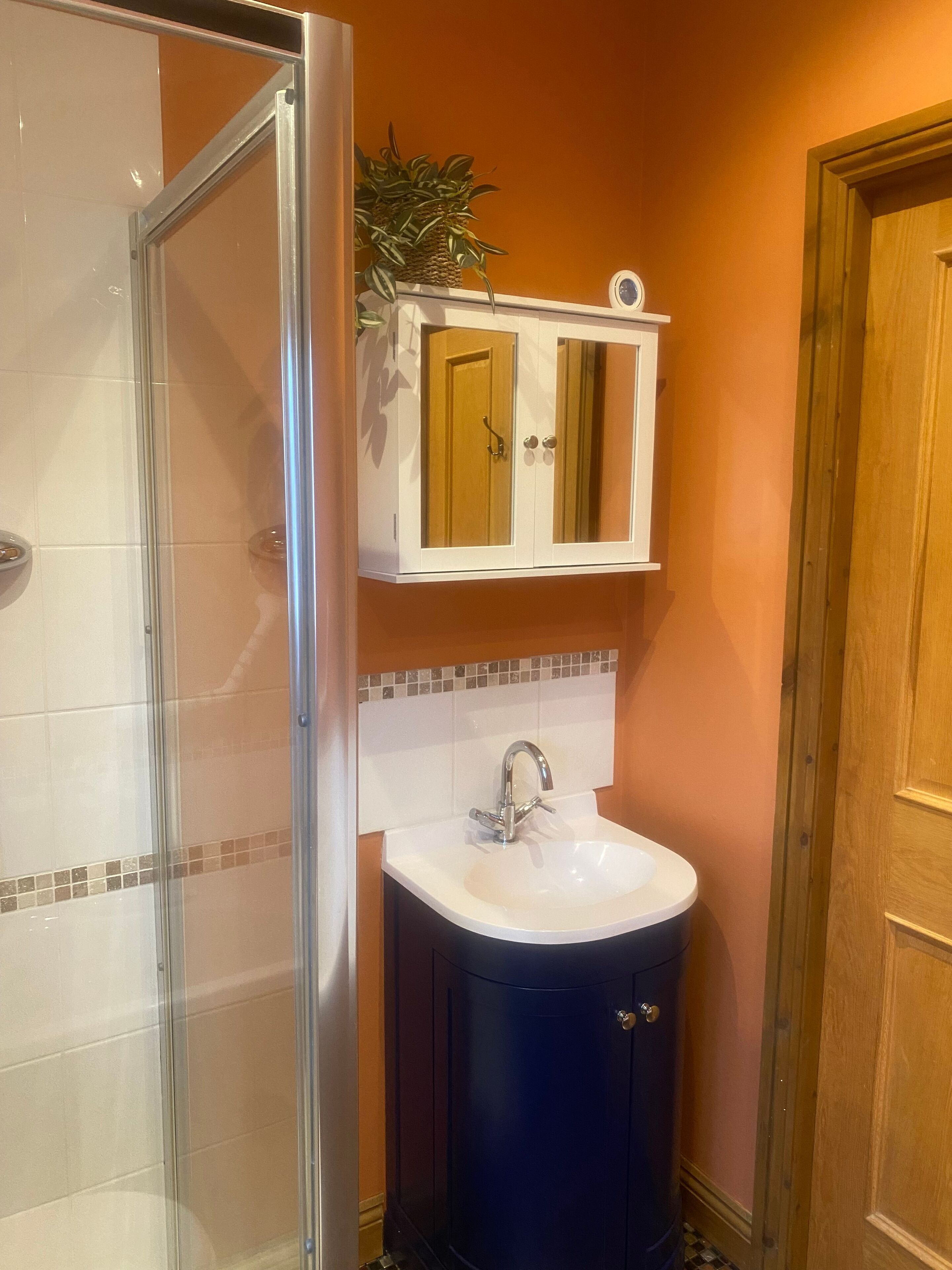 A bathroom with a glass shower enclosure, a white sink with a single faucet, and a wooden door.