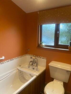 A bathroom with a bathtub, a toilet, and a window with a view of trees. - Luxury log cabin with hot tub- York (York)