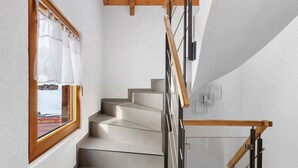 Eine moderne Treppe mit Glastrennwand und Holzhandläufen, die zu einer Aussichtsplattform mit Blick ins Freie führt.