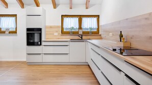 Eine moderne Küche mit Holzbalken, weißen Schränken, einem eingebauten Backofen und einem großen Fenster mit Vorhängen.