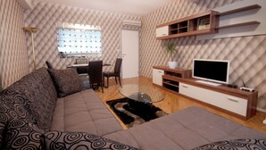 Un salon moderne comprenant un canapé, une table basse en verre, un téléviseur et un petit coin repas avec une chaise et une table.
