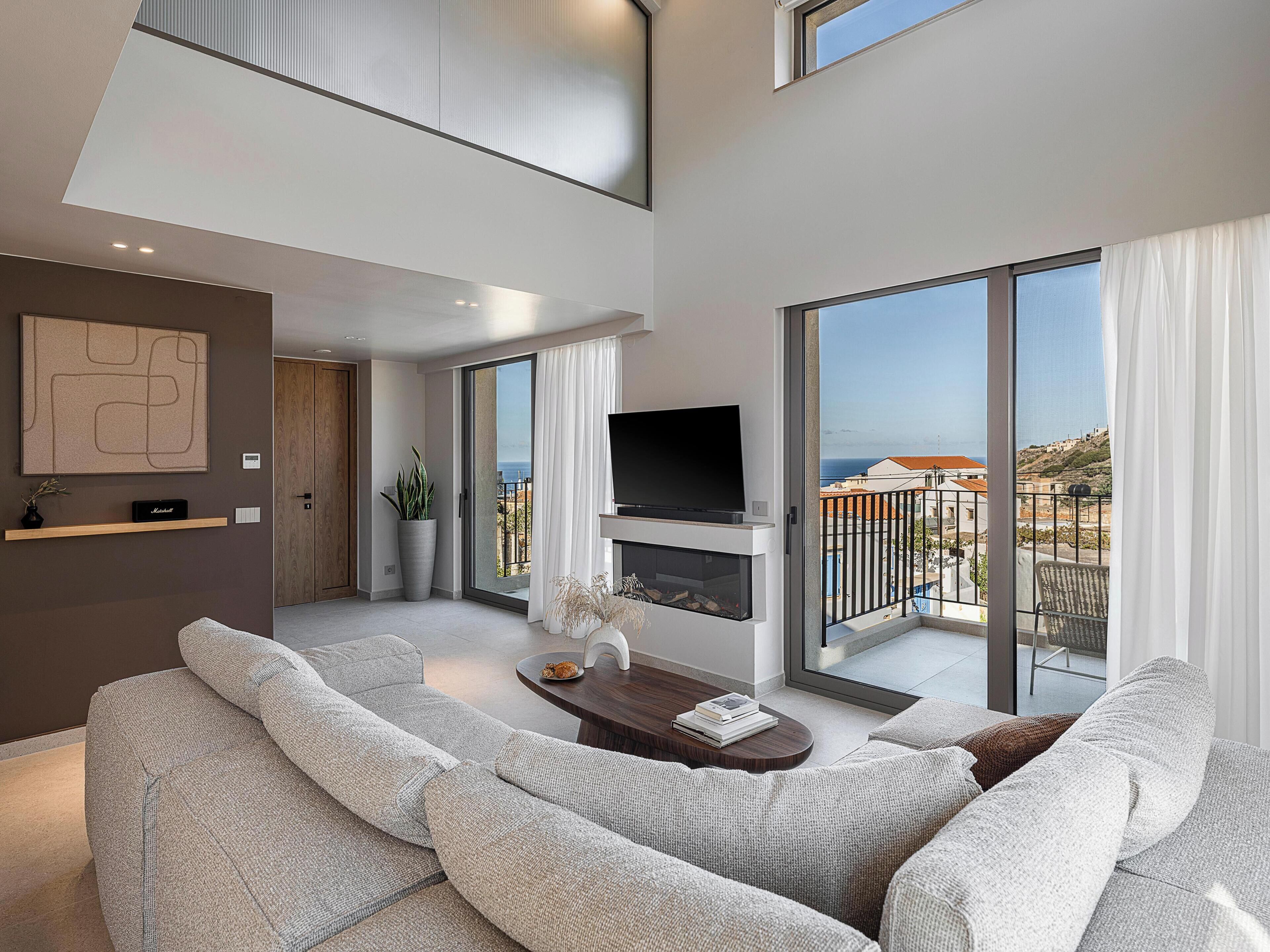 A modern living room with a large sofa, a flat-screen TV mounted on a wall, and a fireplace.