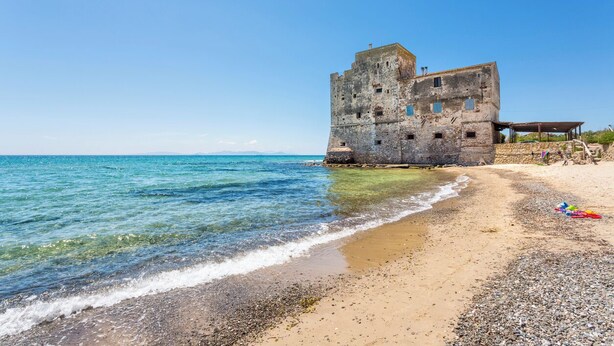 A coastal building with a stone facade, a sandy beach, and clear blue waters. - B&B Litoranea 80 (Follonica)
